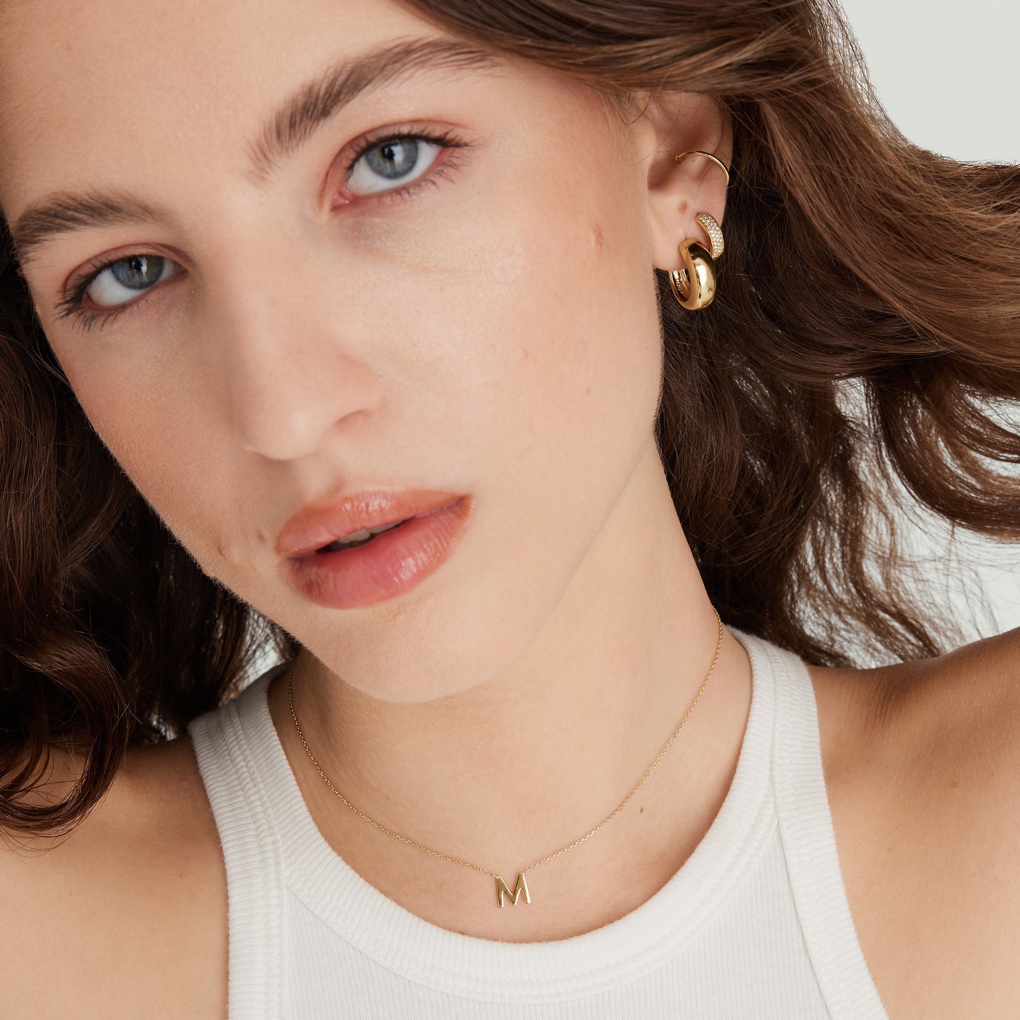 Woman wearing a gold letter necklace and matching gold earrings, highlighting the initial pendant prominently against her neck.