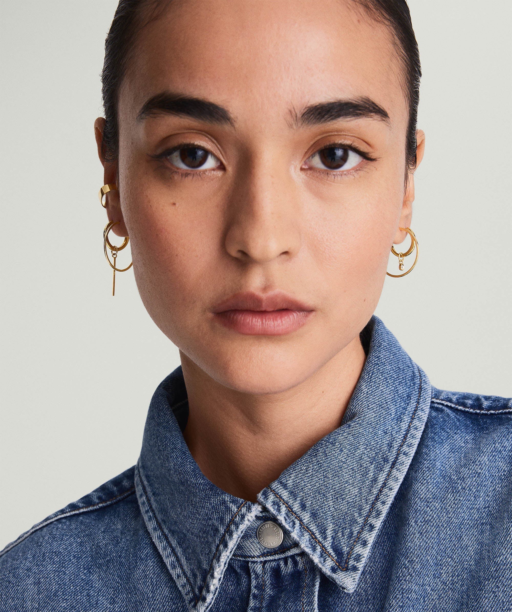 Woman with short dark hair wearing a denim jacket, showcasing Large Hoops in 14k solid gold.