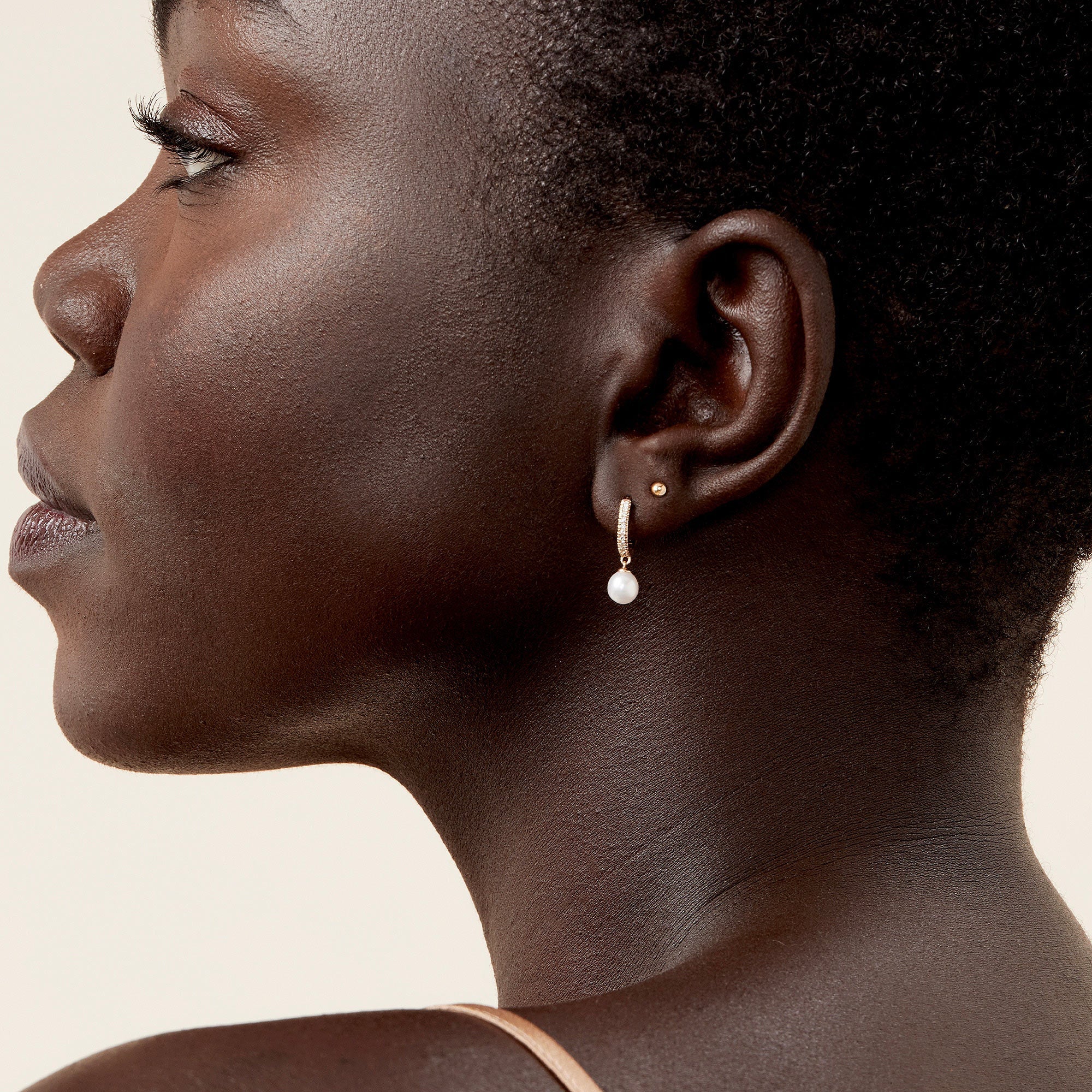 PavÃ© Diamond Pearl Huggies: close-up of a woman with short hair wearing handcrafted 14k gold earrings featuring 22 diamonds in a pavÃ© setting and a freshwater pearl.