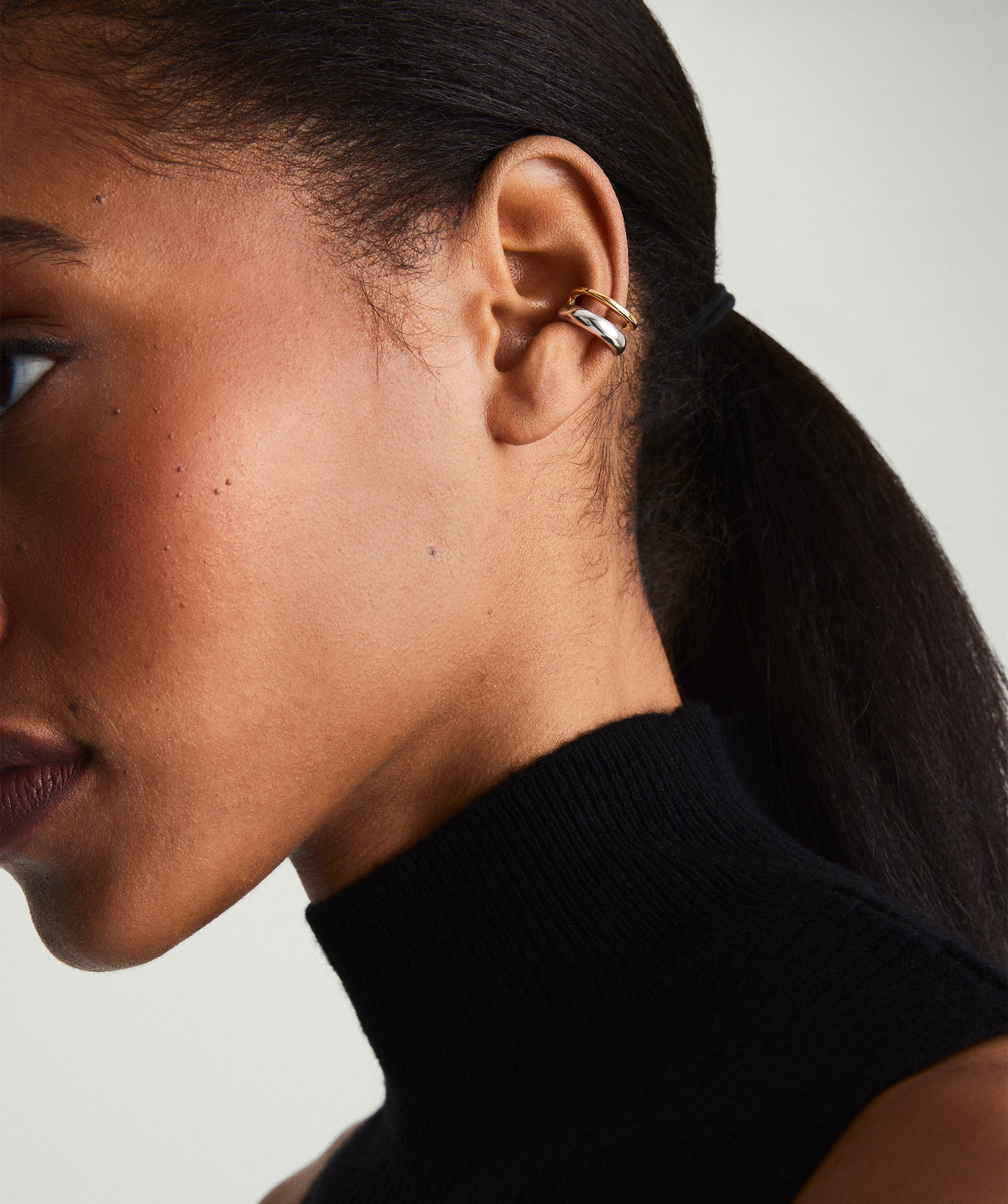 Woman wearing a black turtleneck and ponytail, showcasing the Duet Mixed Ear Cuff with two stacked rings in gold vermeil and sterling silver.