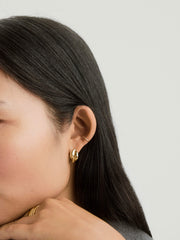 Close-up of a woman's ear wearing Brioche Hoops, gold earrings designed with a knot-like pattern, ideal for everyday fashion.