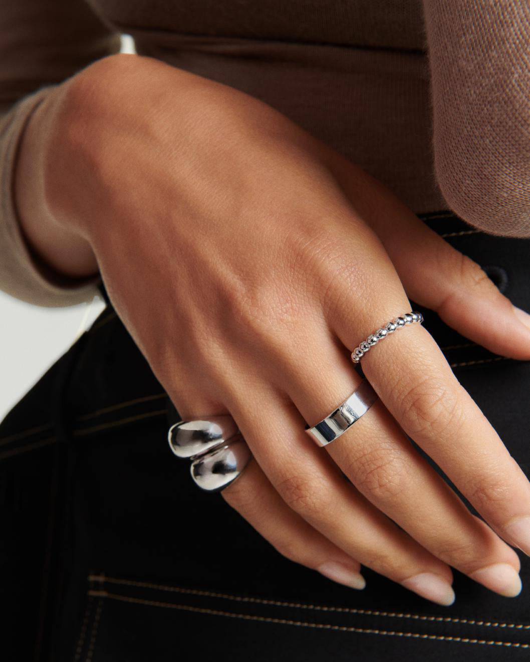 Close-up of a hand adorned with multiple silver rings, prominently featuring the bold DÃ´me Ring, ideal for creating a stylish, stacked look.