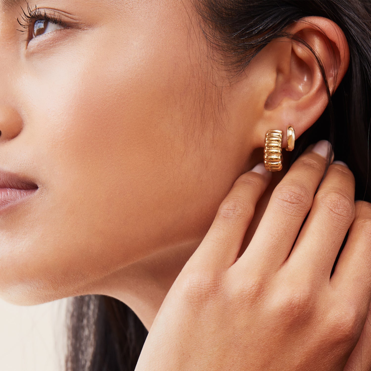 Woman wearing Charlotte Bold Hoops, touching her ear, showcasing the gold ring on her finger, inspired by the iconic French dessert.