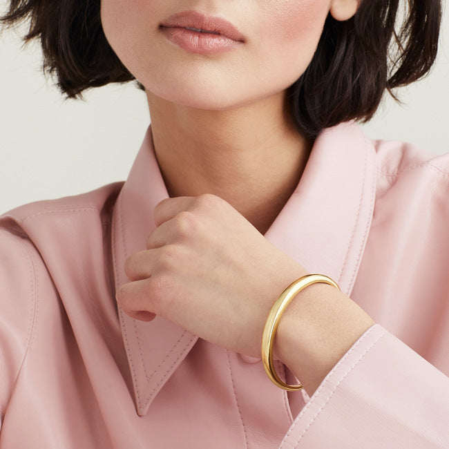 Woman wearing a pink shirt displaying a gold DÃ´me Cuff Bracelet on her wrist.