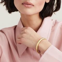 Woman wearing a pink shirt displaying a gold DÃ´me Cuff Bracelet on her wrist.
