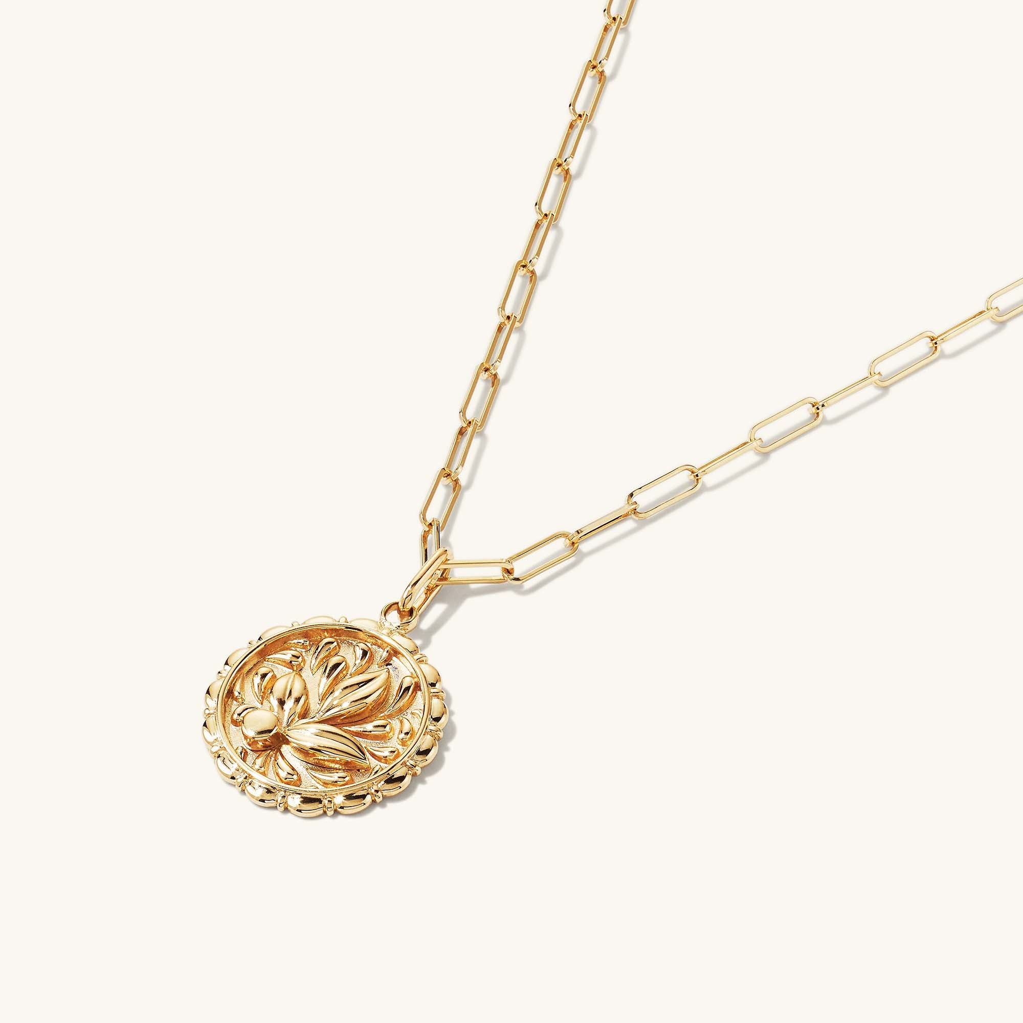 Balance: Terra Coin Charm Pendant, a close-up of a gold necklace with a round medallion featuring intricate design, inspired by Greek Goddess Gaia.