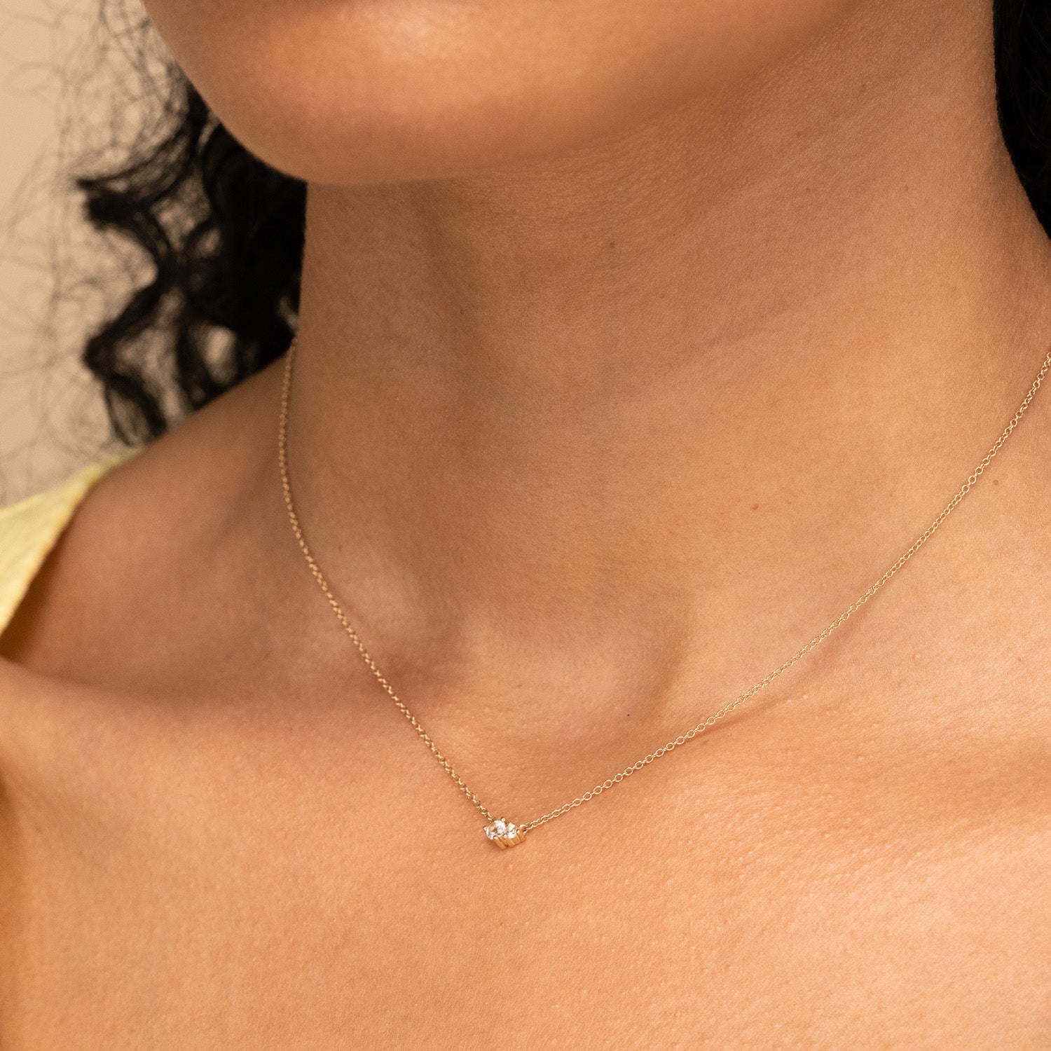 Woman wearing the Hue Necklace, a handcrafted 14k solid gold piece with genuine white topaz gemstones, shown close-up on her neck.