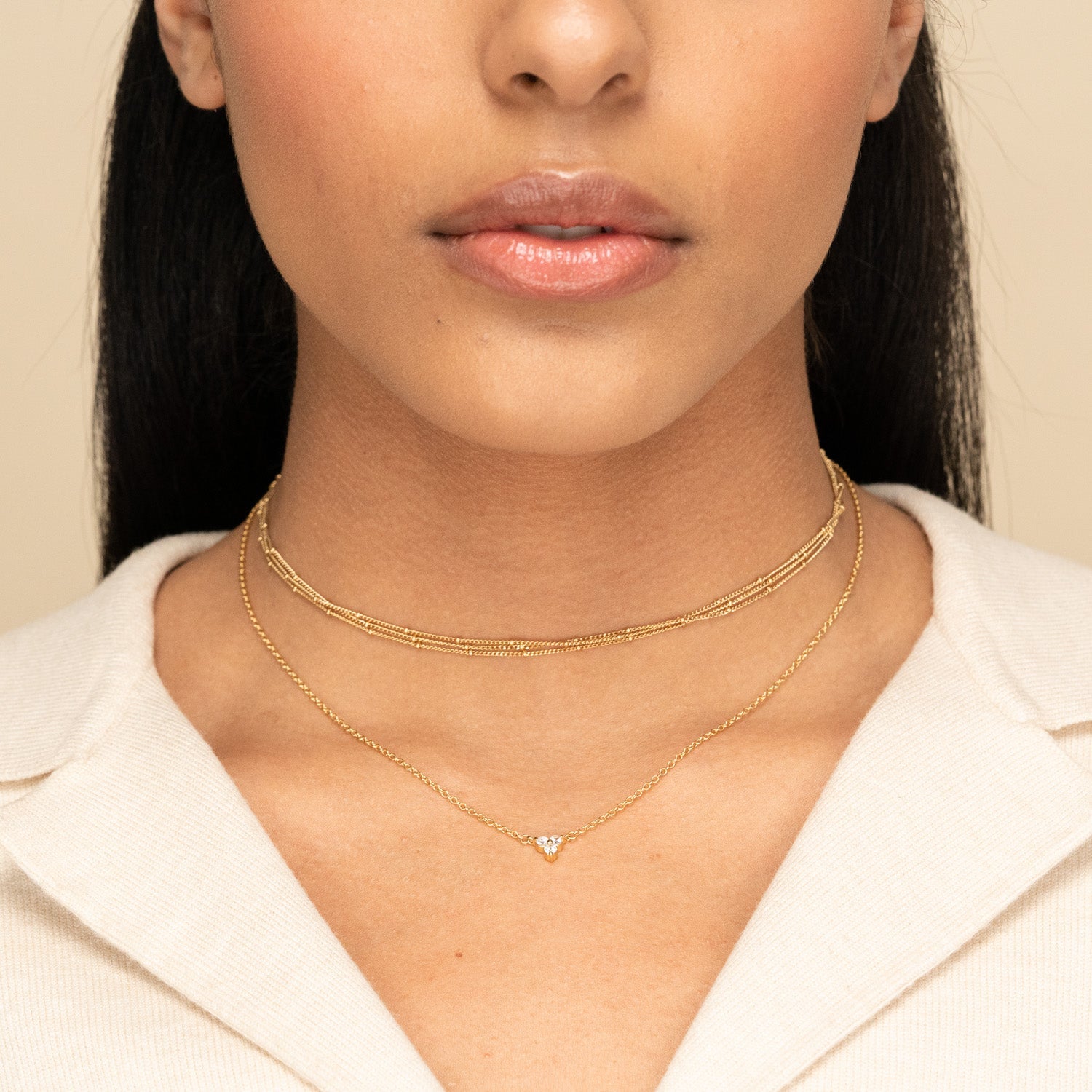 A woman wears the Lotus Necklace, featuring a layered gold choker and a pendant with three stones, highlighting its versatile elegance against a collared top.
