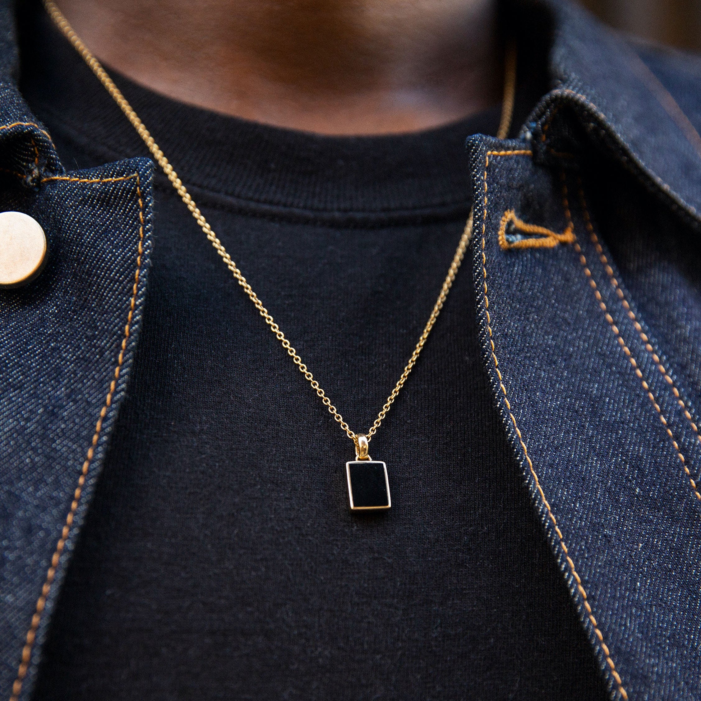 Black Onyx Pendant Necklace worn by a person, featuring a black rectangular pendant on a gold chain, styled over a black shirt.