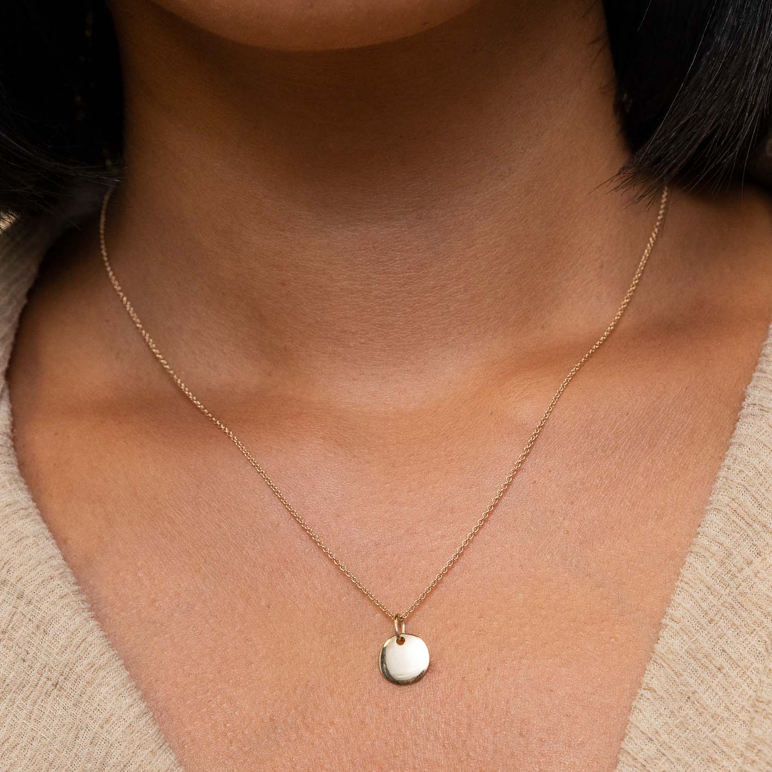 Woman wearing an Engravable Charm necklace featuring a silver circle pendant on a chain, close-up of neck and pendant.