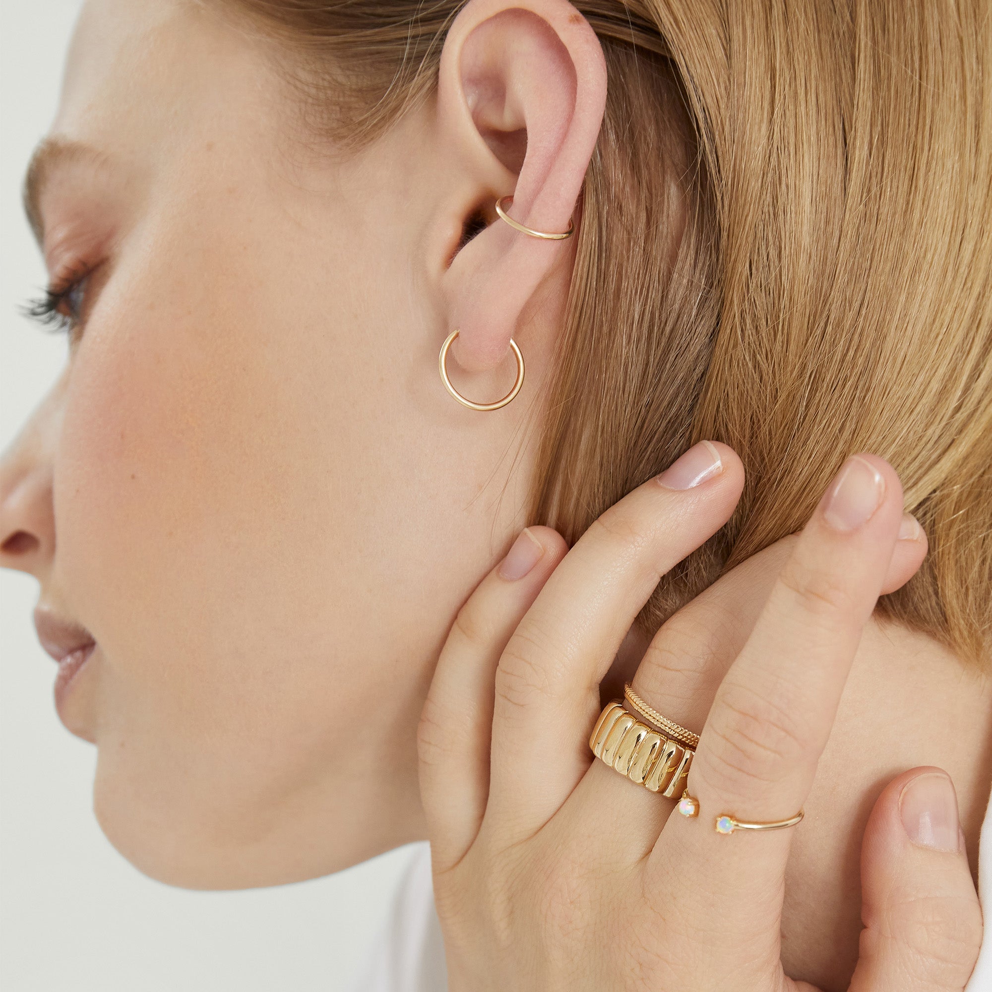 Woman wearing the Charlotte Bold Ring on her finger, showcasing its elegant design beside a gold hoop earring in her ear.