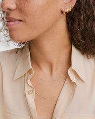 Baby Box Chain Necklace elegantly layered around neck, showcased with light beige shirt and gold hoop earrings, highlighting its delicate, light-catching design.