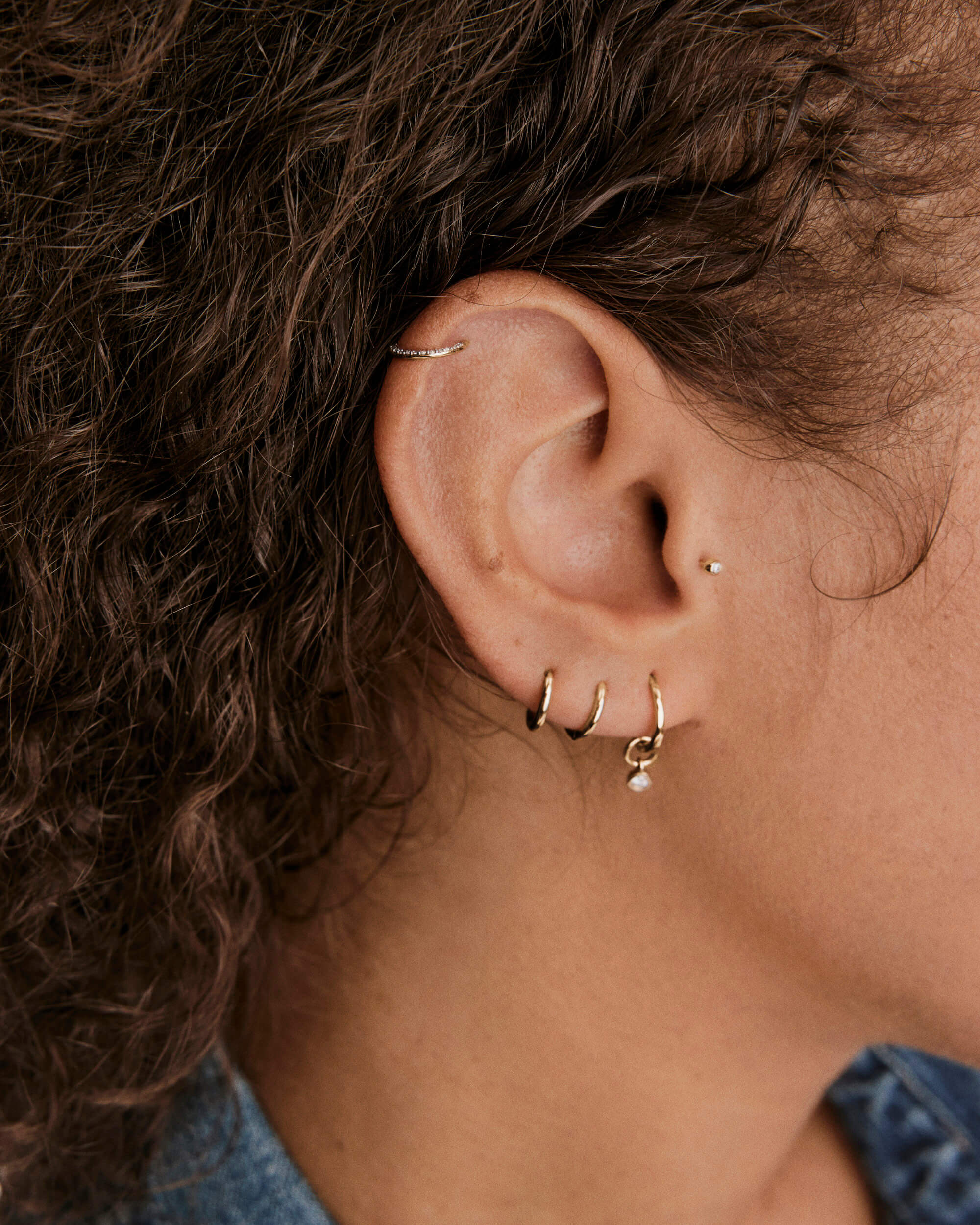 Close-up of a pierced ear featuring the Cartilage PavÃ© Diamond Mini Hoop in textured gold, worn on the helix, with other small gold hoops and a stud.