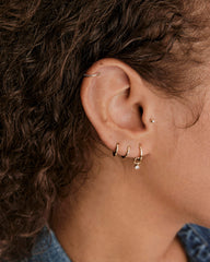 Close-up of a pierced ear featuring the Cartilage PavÃ© Diamond Mini Hoop in textured gold, worn on the helix, with other small gold hoops and a stud.