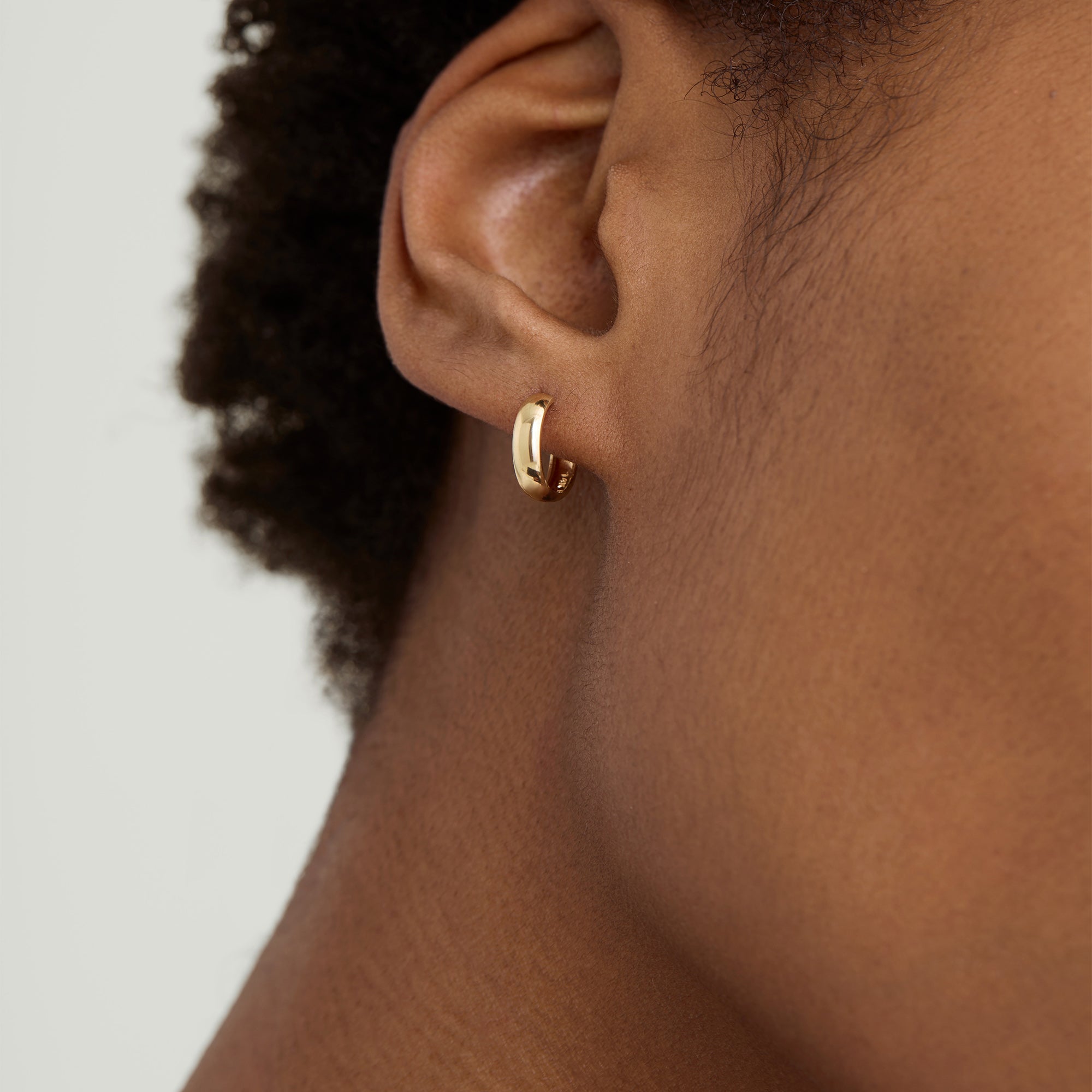 Single Bold Huggie Hoop on a person's ear, showcasing a handcrafted, recycled 14k solid gold hoop earring, highlighting its bold, fashion-forward design.