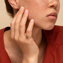Close-up of a woman's face showcasing a handcrafted 14k gold signet ring with a customizable bezel surface for engraving.