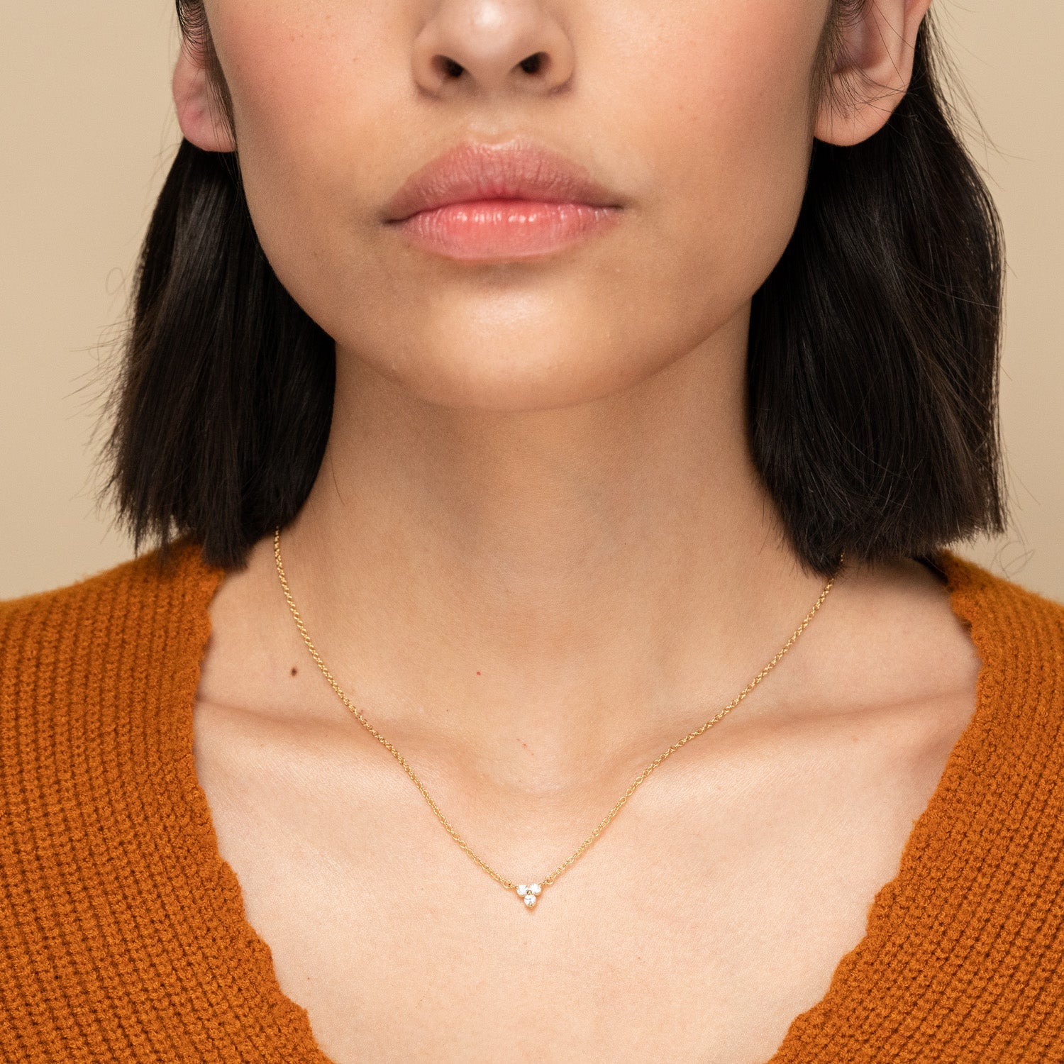 Close-up of a person wearing the Lotus Necklace, featuring a fine gold chain with a triangular cluster of three small stones, complementing a scalloped neckline.