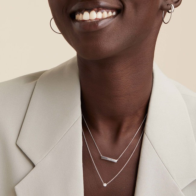 Woman smiling, wearing the Horizontal Engravable Bar Necklace and earrings; the necklace features a sleek, minimal 14k gold bar, customizable with up to seven letters.